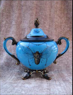 A whimsical blue tea set sugar bowl with a curved decorative handle, adorned with a large golden cicada and hand painted details