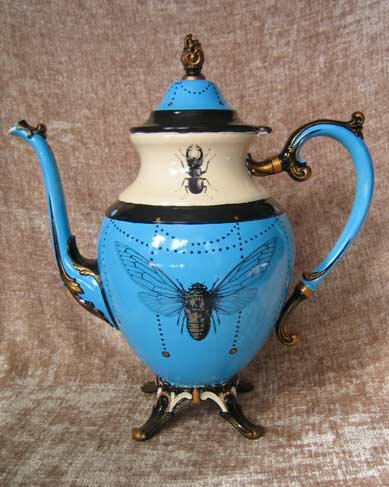 A whimsical blue teapot with a long curved spout and decorative handle, adorned with insects and hand painted details, a large golden cicada is the main decorative element