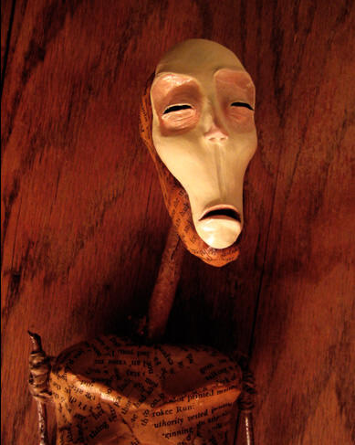A paper mache doll made of antique book pages and sticks, with a long pale face, squinting thoughtfully into the distance