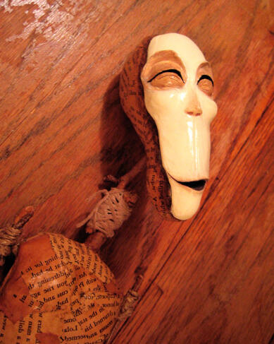 A paper mache doll made of antique book pages and sticks, with a long pale face, squinting joyfully upward
