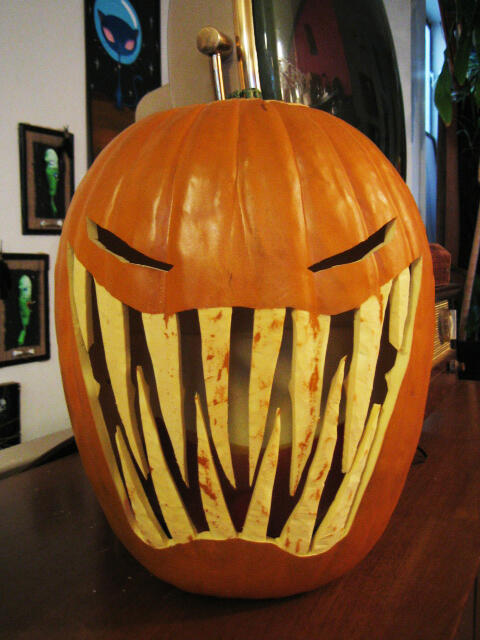 Tall elongated Halloween pumpkin decoration with a huge toothy grin, long sharp teeth, and tiny squinting eyes.