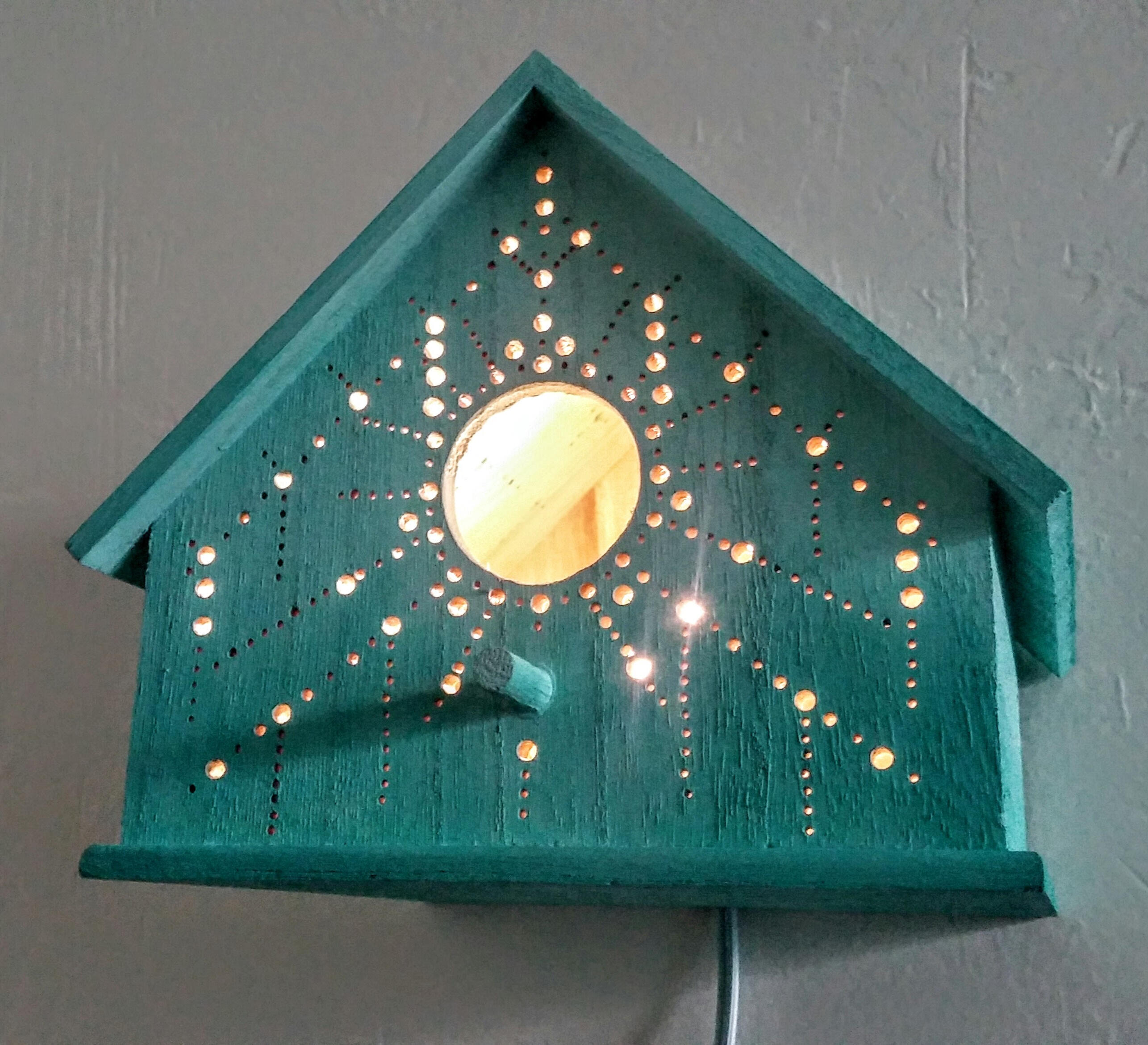 Turquoise birdhouse lamp decorated with perforated patterns that glow with warm yellow light from inside.