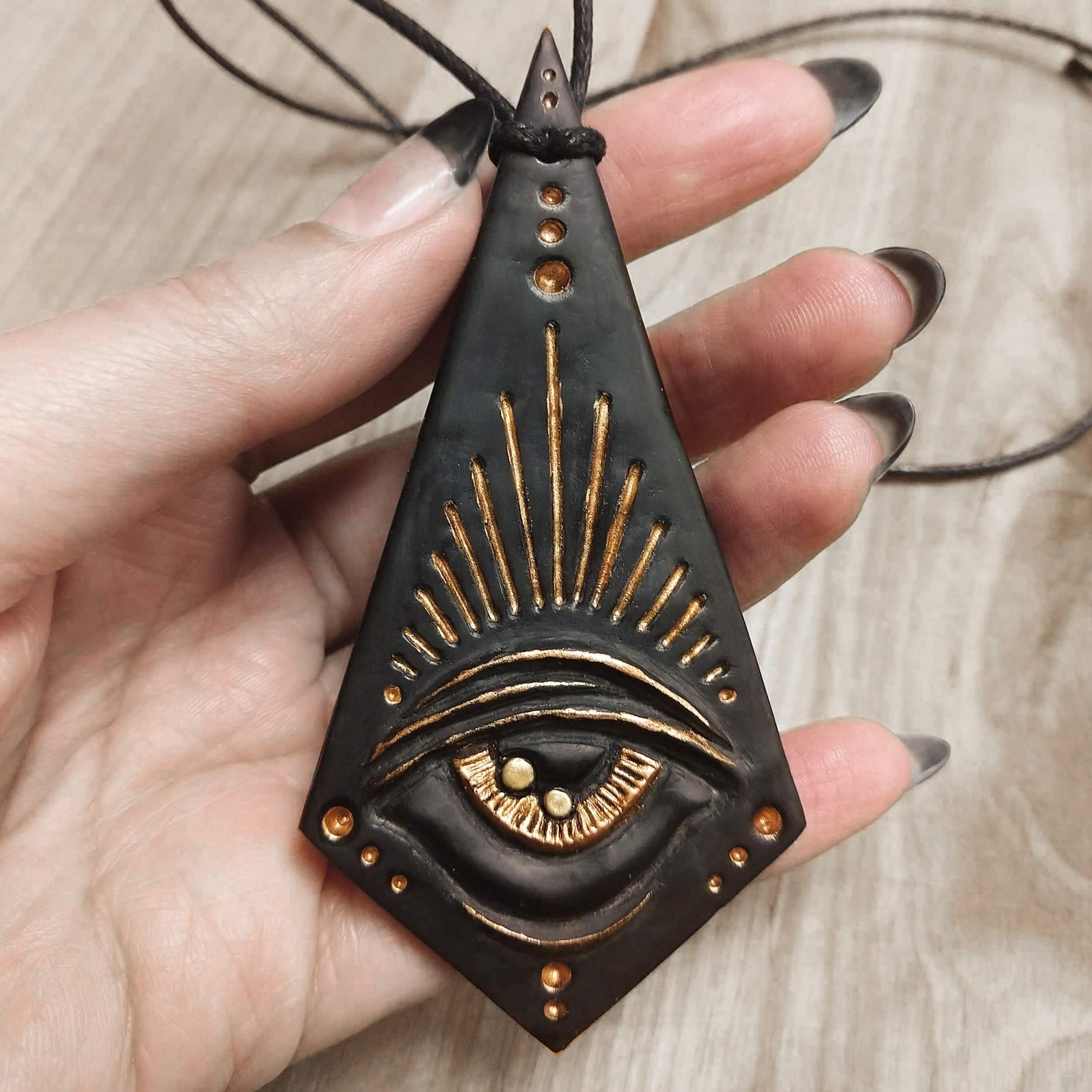 Matte black resin angular pendant featuring a large golden eye surrounded by radiating gold rays.