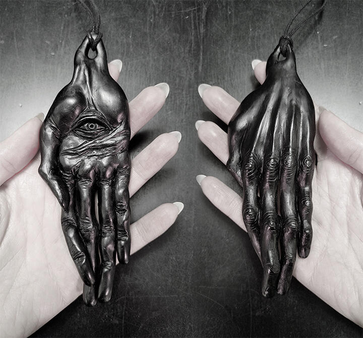 Oversized matte black resin talisman depicting a thin gnarled witch's hand with a spooky eye in the palm