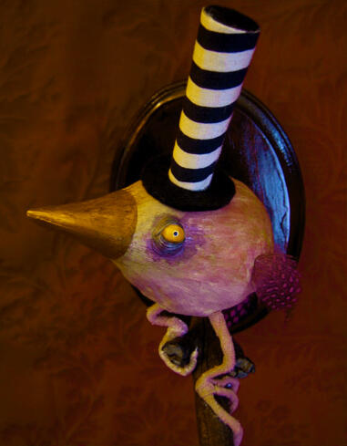 A fat pink bird in the shape of a teardrop, with beady yellow eyes, tiny feathered wings and tail, perched on a branch sprouting from a wooden plaque on the red wall background, and wearing a very very tall black and white striped tophat.