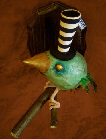 A fat green bird in the shape of a teardrop, with beady yellow eyes, tiny feathered wings and tail, perched on a branch sprouting from a wooden plaque on the red wall background, and wearing a very very tall black and white striped tophat.