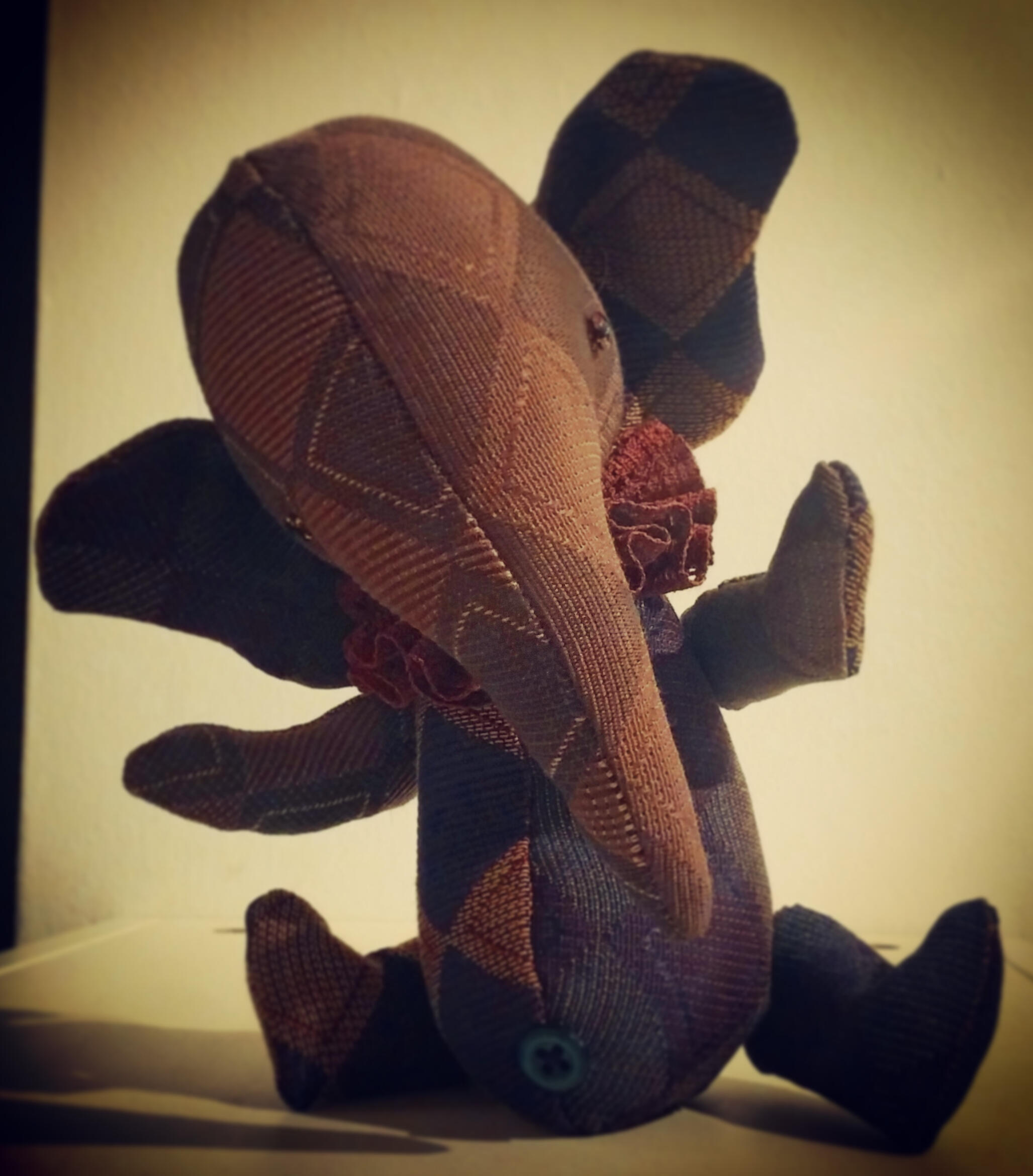 A whimsical stuffed elephant doll made out of vintage harlequin fabric in shades of purple with a ruffled collar